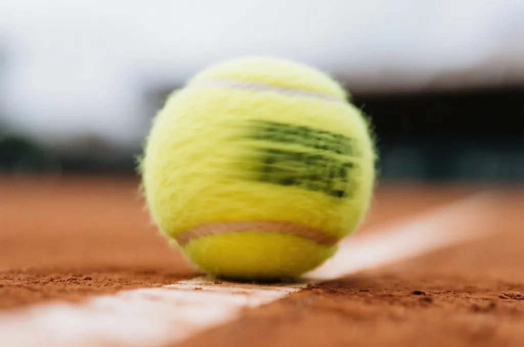 Close-up of a tennis ball spinning near the white baseline of a clay court, dynamic action shot